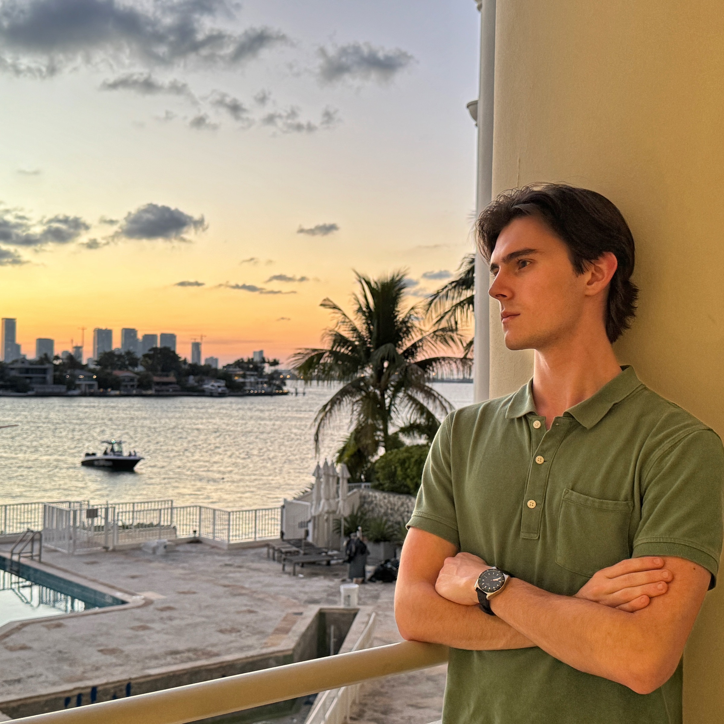 Matthew Pulcini on a waterfront balcony at sunset with the Miami skyline in the distance